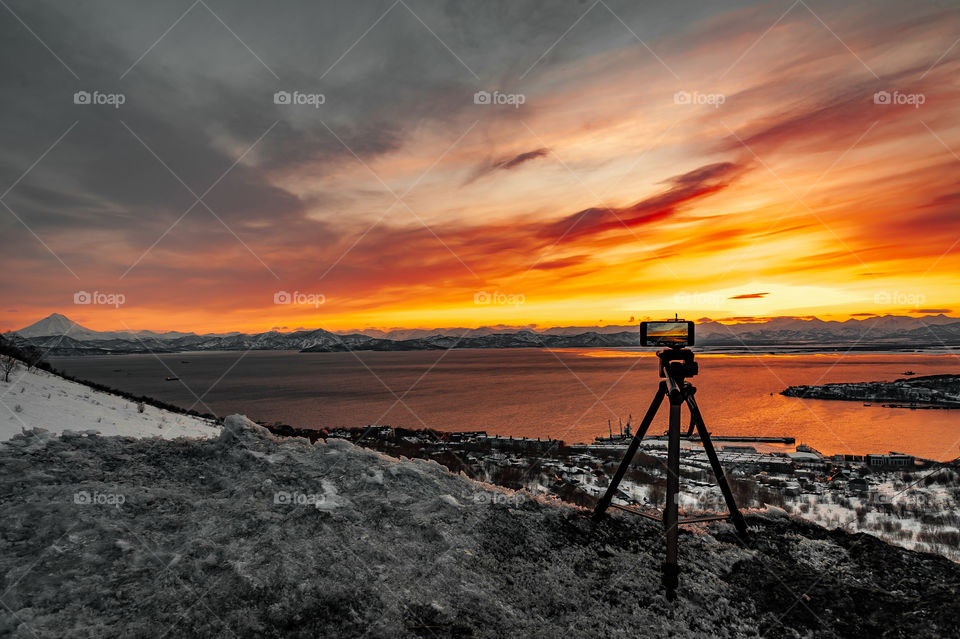 cold winter Kamchatka evening on a tripod there is a phone that is recording time lapse of sunset