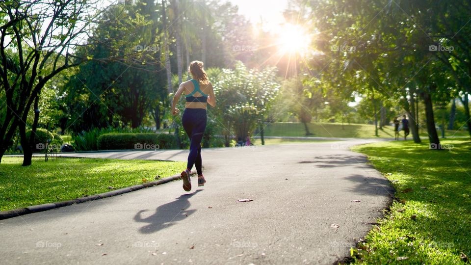 Beautiful woman jogging in the park with sun rays in the morning 