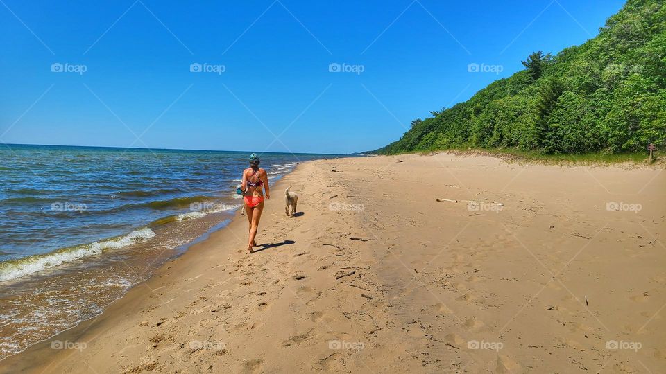 woman and dog walk on secluded lake Michigan Beach