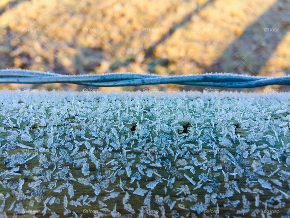 Minimalistic closeup of frost crystals on a wooden fence, twisted wire and blurred background of shadows on dry field grass
