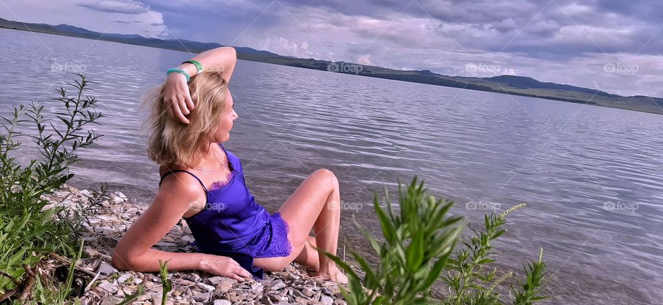 девушка лежит в фиолетовом сарафане на берегу озера