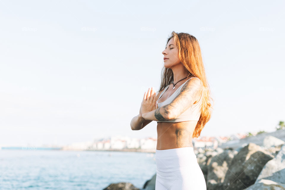 Young fit beautiful woman with long hair in white sport clothes practice yoga and meditation on the sea beach