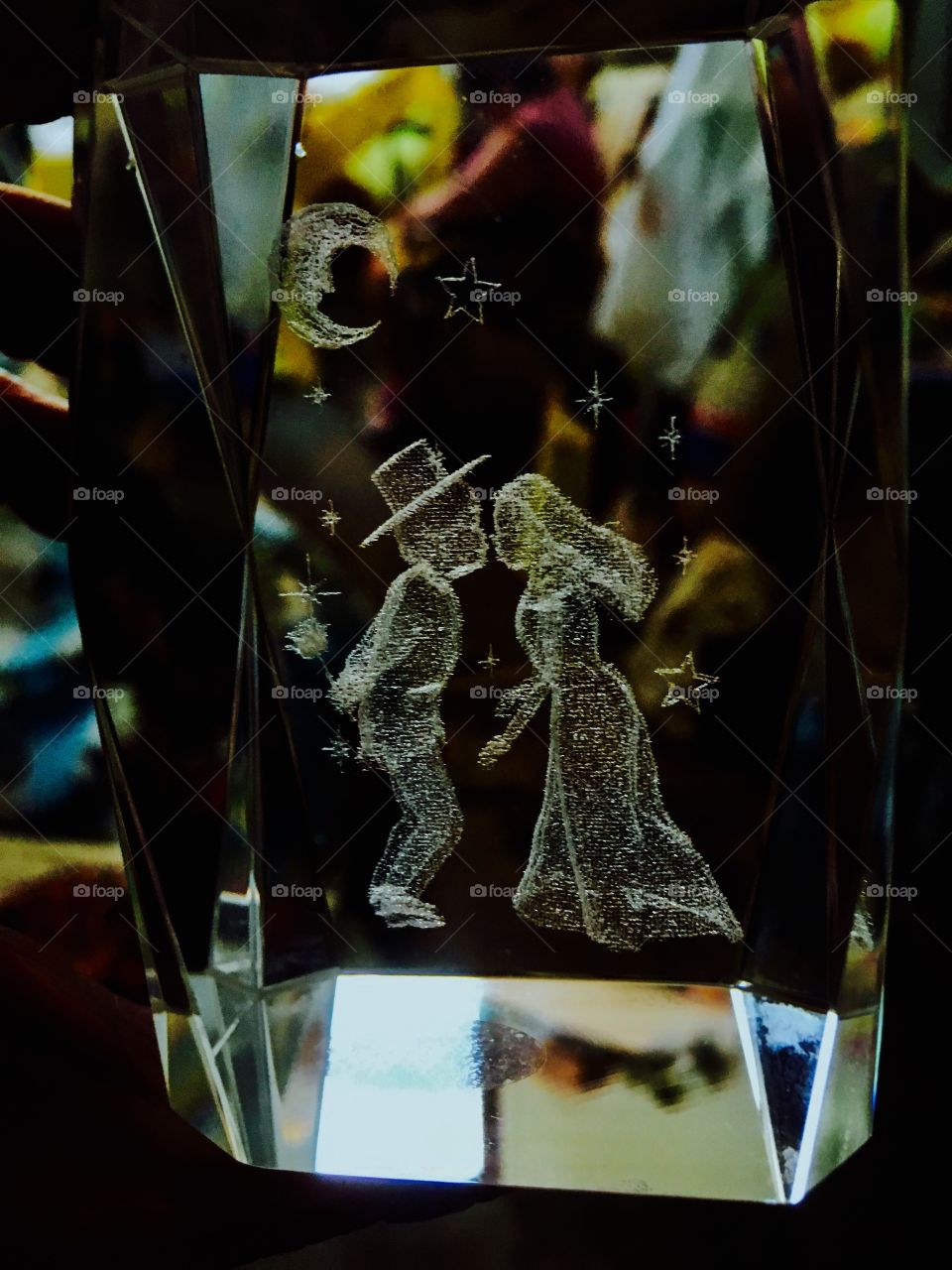 Blurred light and color reflections off of glass etched paperweight depicting an old fashioned couple under the moon and stars
