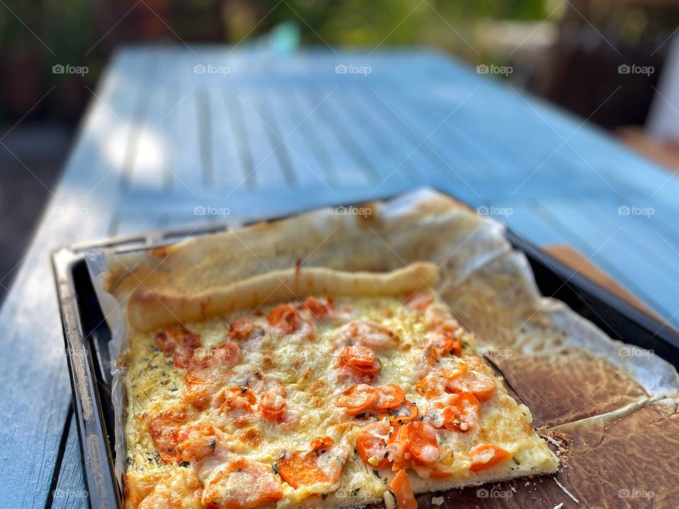 Pizza with vegetables stands on a blue table in the garden