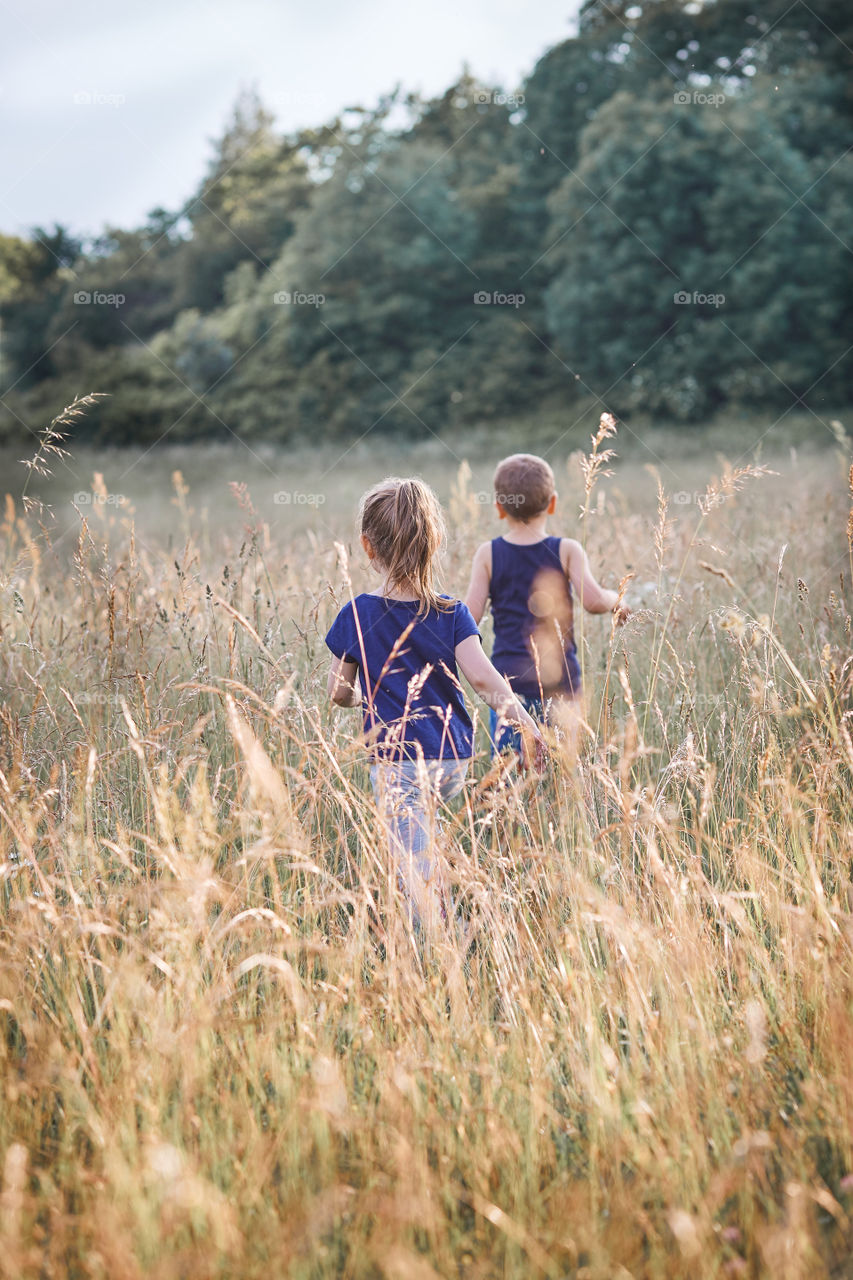 Little happy girl walking through a tall grass in the countryside. Candid people, real moments, authentic situations