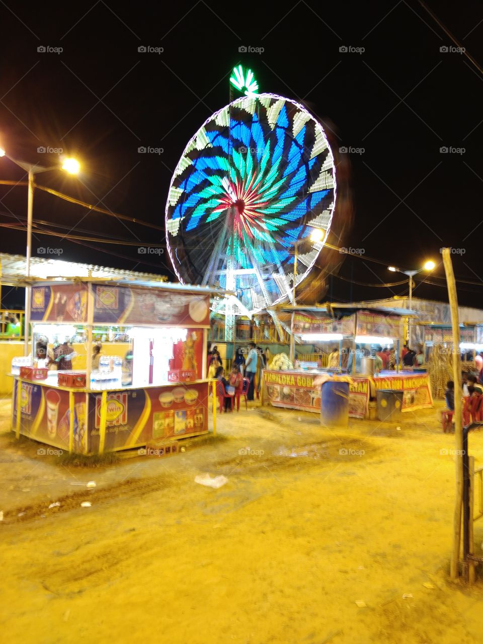 giant wheel in a fare and stalls around for food and refreshment. family and friends enjoyment place. children love rides and eating here.