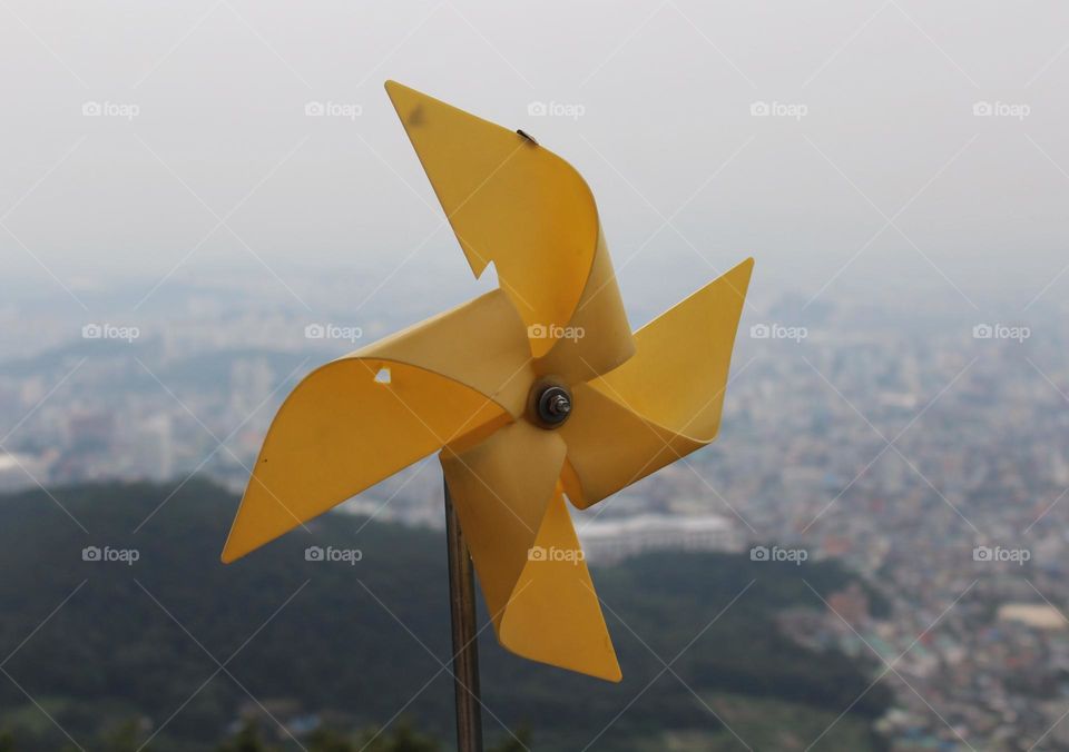 A yellow windmill on the backdrop of a major Korean city.