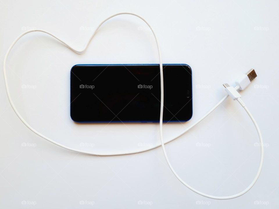 flat lay with smartphone and its cable in the shape of a heart