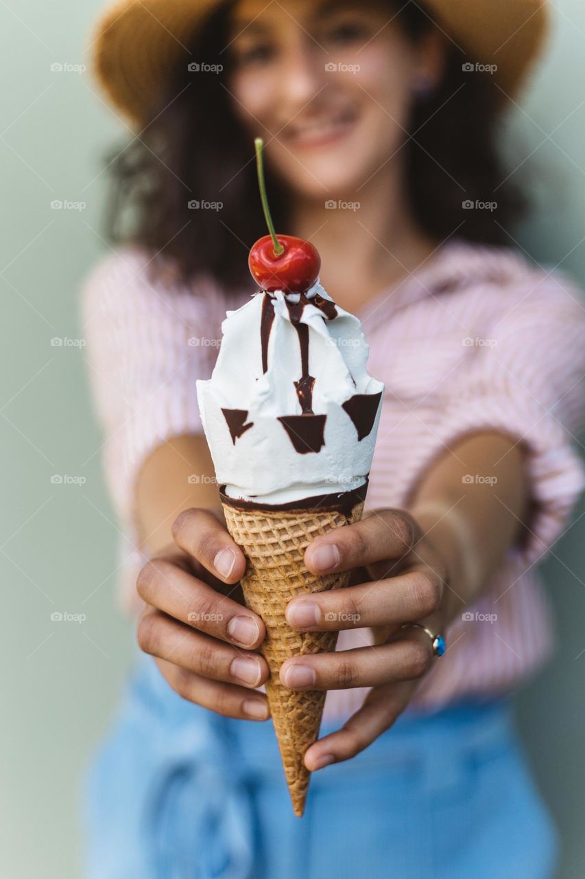 Young woman colorfully dressed, holding a delicious icecream with a cherry on top, on a hot summer day.