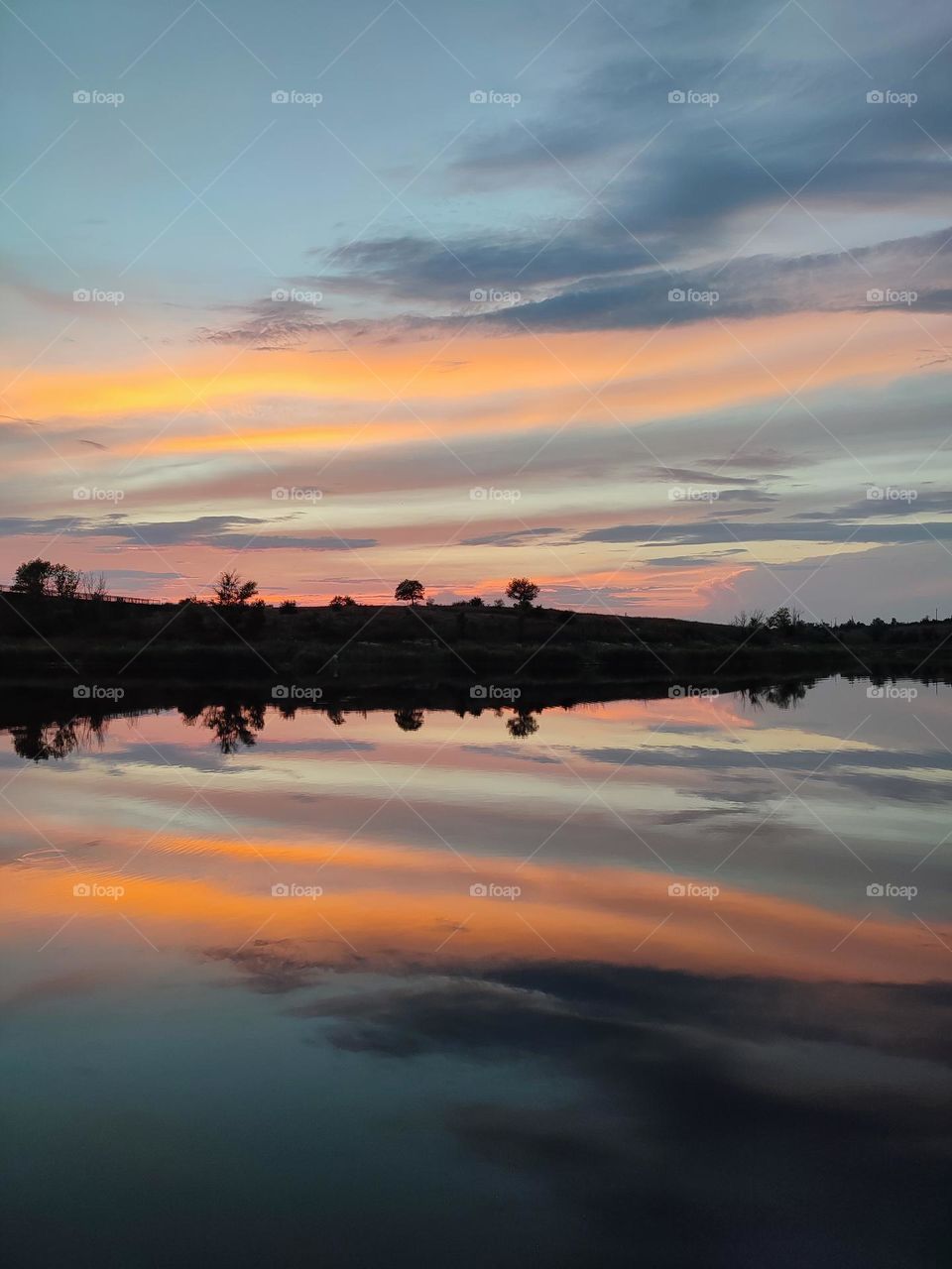 Beautiful colorful sunset on the water. Orange and blue clouds reflection on the calm river's water. Horizon, skyline, beautiful summer landscape