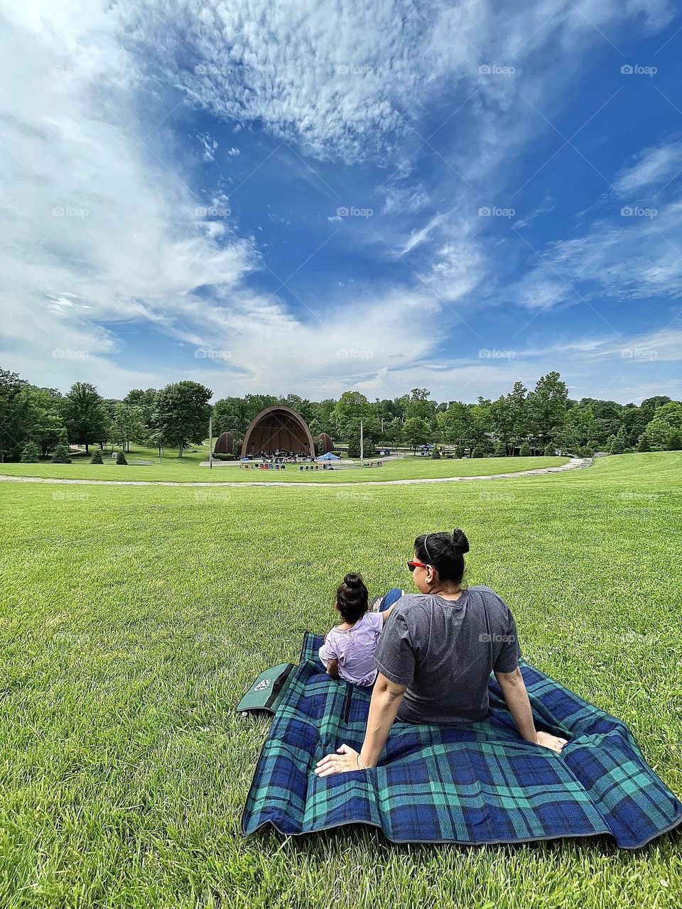 Mother and daughter sit on the grass on a blanket, taking in the scenery with toddler, moments of happiness with a toddler, relaxing moments in life, enjoying life with children 