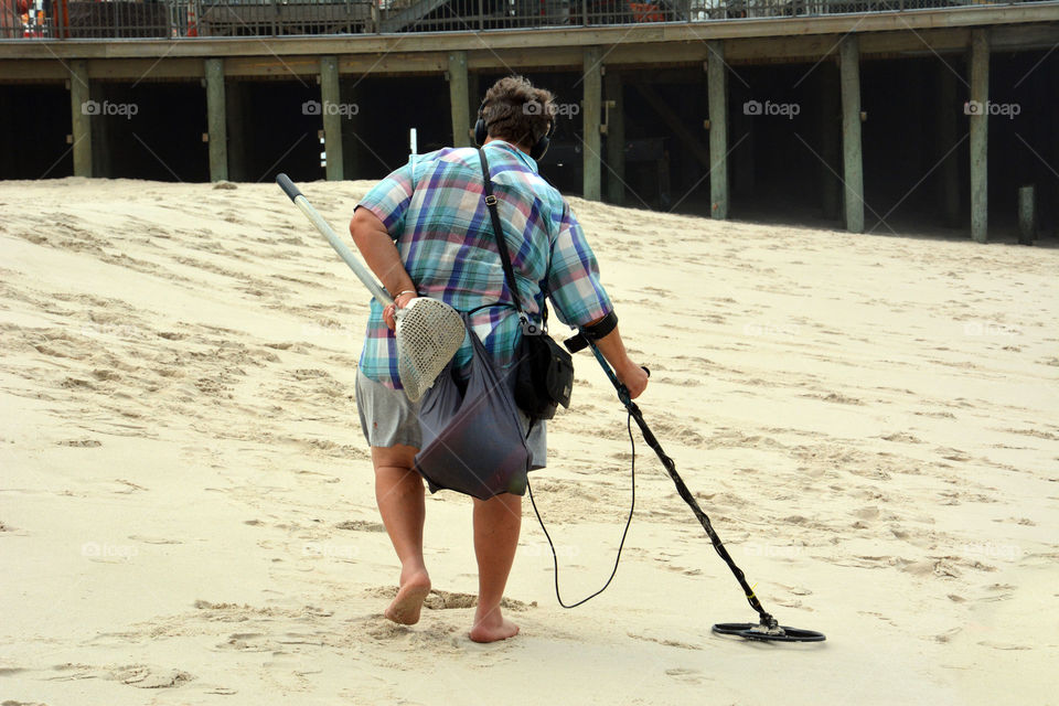 An unrecognizable man scans the beach sand with a metal detector
