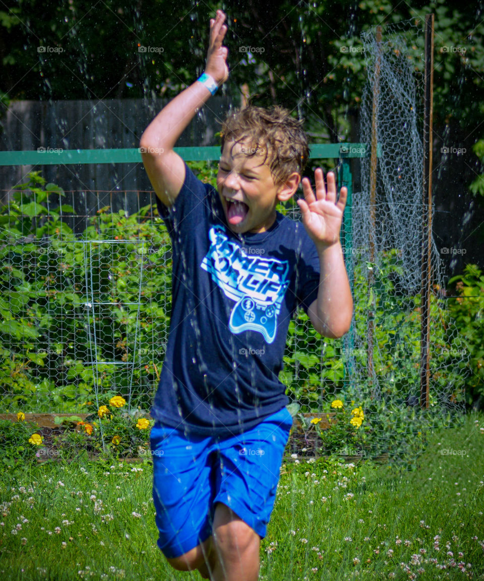 Boy laughing and playing in the sprinkler