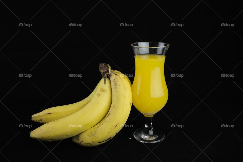 Bananas with glass beaker with juice on black background