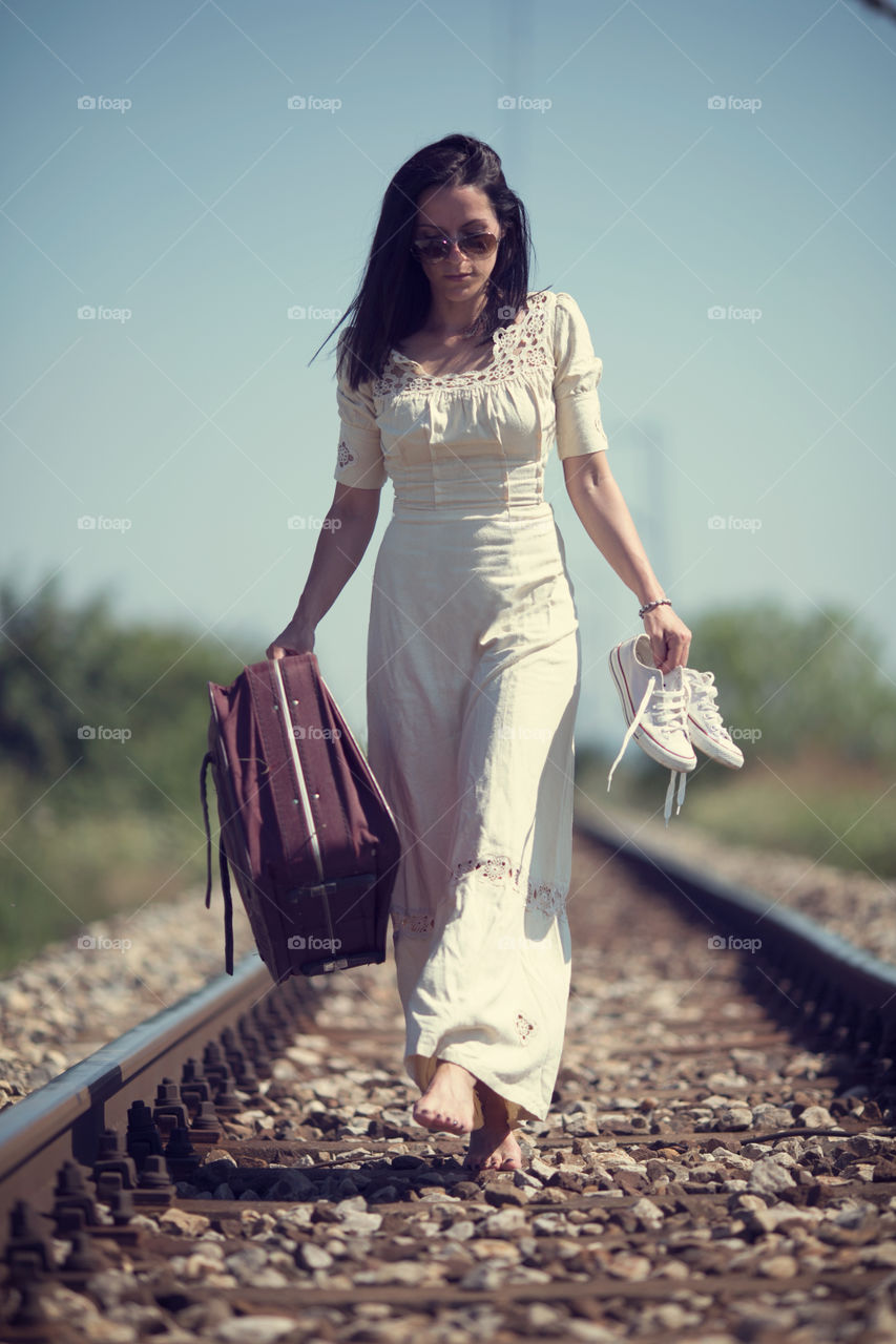 Woman walking on rail track with backpack and shoes in hand