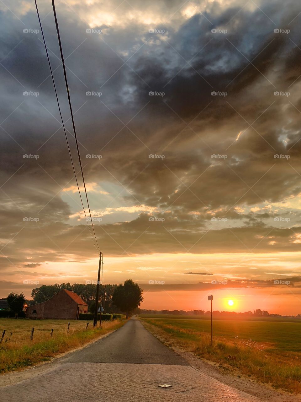 Countryside sunrise landscape with electricity lines running along a rural road passing by a farm