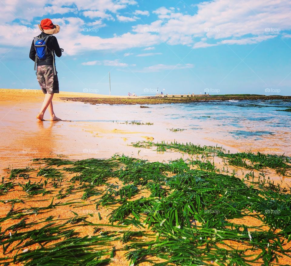 Boy walking on beach with green seaweed 
