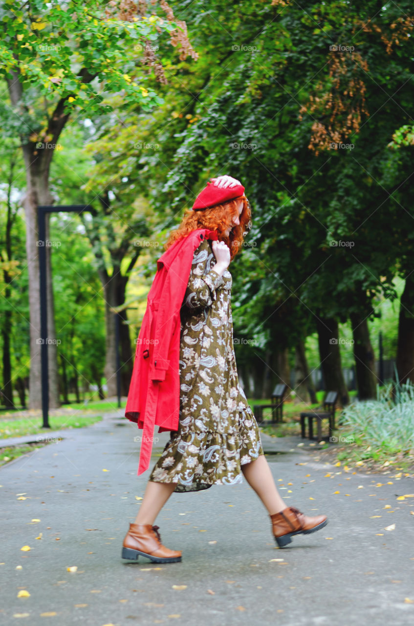 Young happy woman with red hair, freckles in a red beret and a coat walking in autumn park. Fall cold season