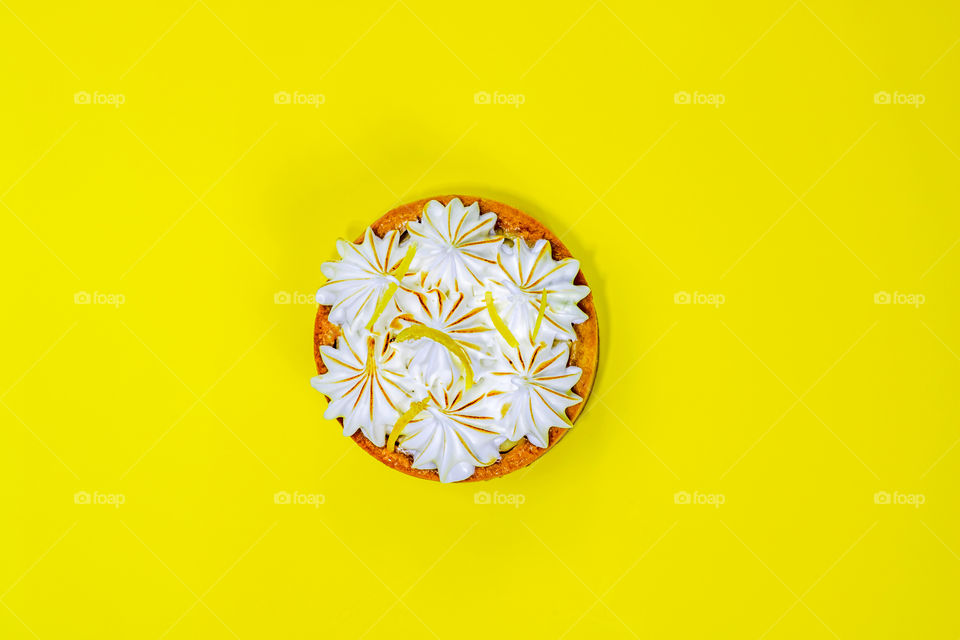 Top view to one meringue lemon tart on yellow background with copy space.