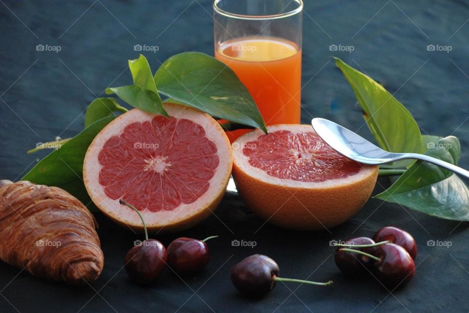 Healthy breakfast with fruit and juice , diet , croissant, orange juice, cherries , green leaves, grapefruit , spoon