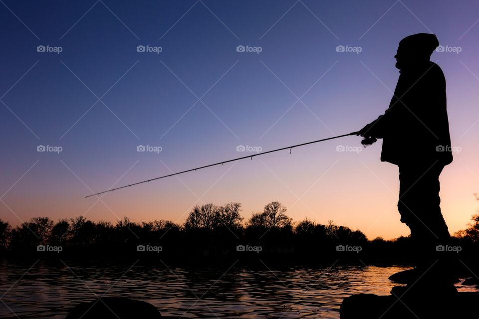Silhouette of a fisherman. Silhouette of a sports fisherman standing on a rock and fishing on a bay in Blekinge, Sweden at sunset time