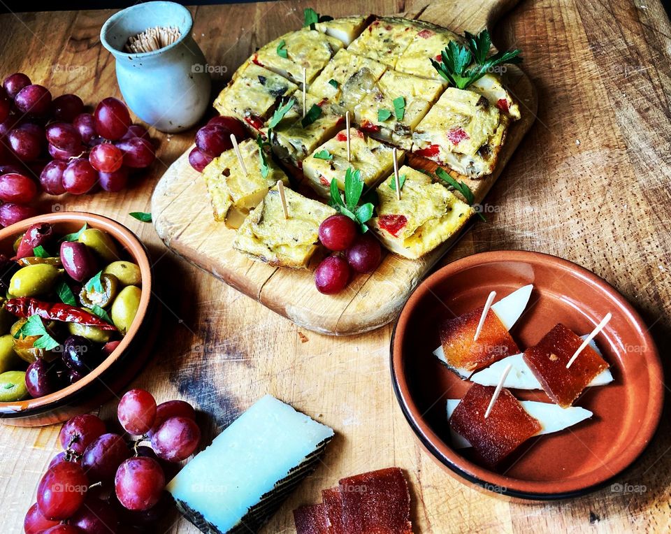 Tapas at home with home cooked tortilla espanola, marinated olives, cheese and fruit in a sunny kitchen.  