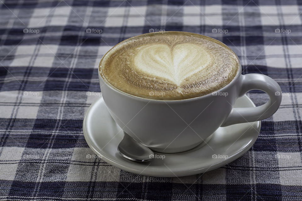 Hot coffee Espresso topped with a heart-shaped milk in white glass On the table with chintz Scott.