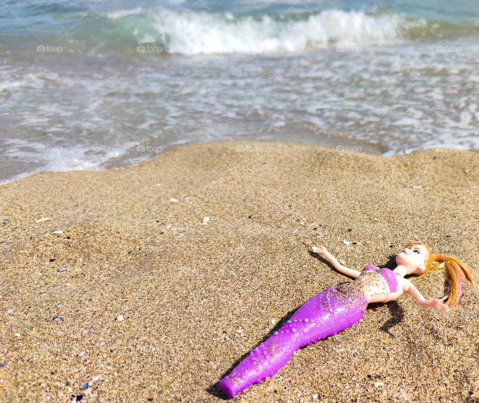 A doll in purple making sunbath on the beach