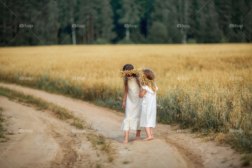 Little sisters on the sand road through the rye field 