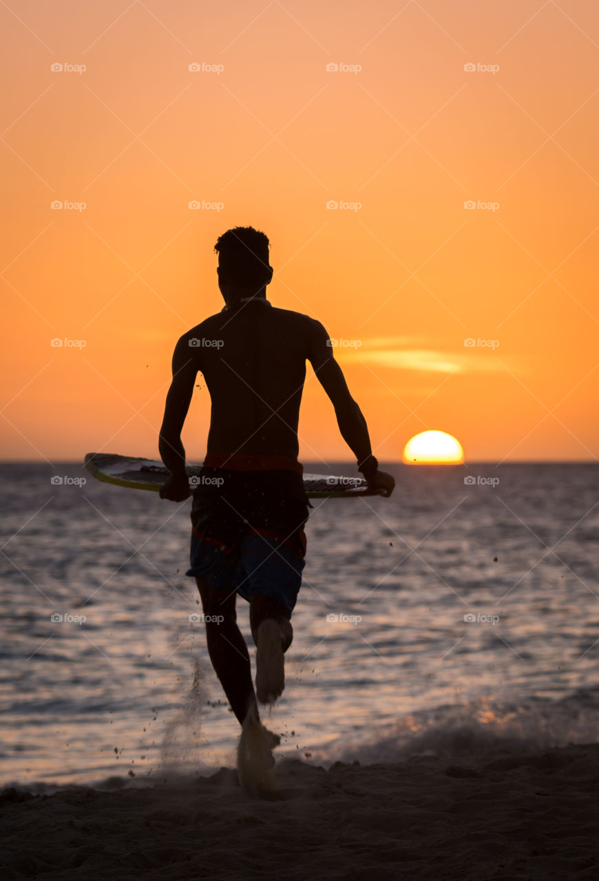 Silhouette of man with surfboard at beach during sunset