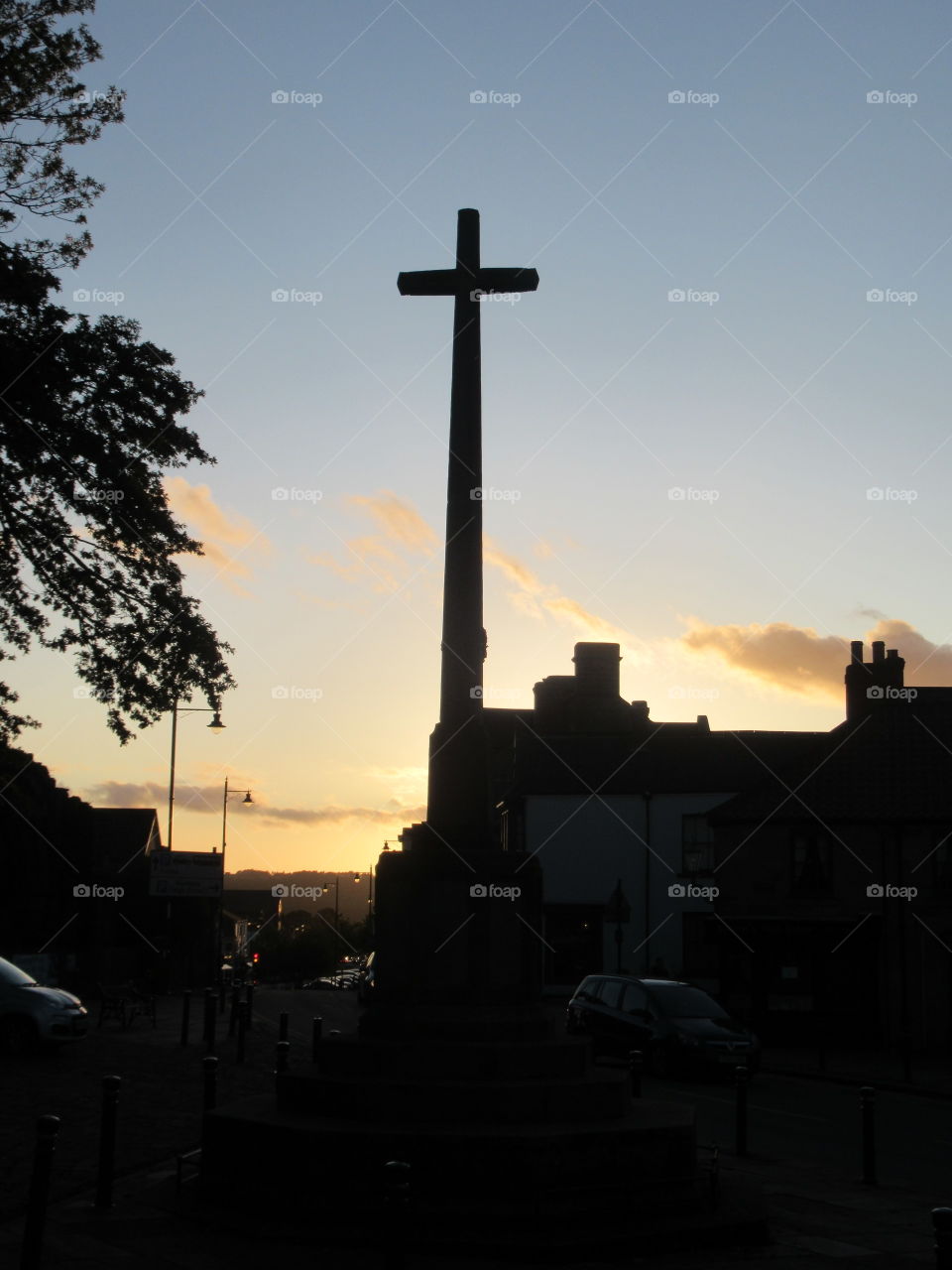 War memorial at sunset with buildings tree and a cross darkened with the autumn sky