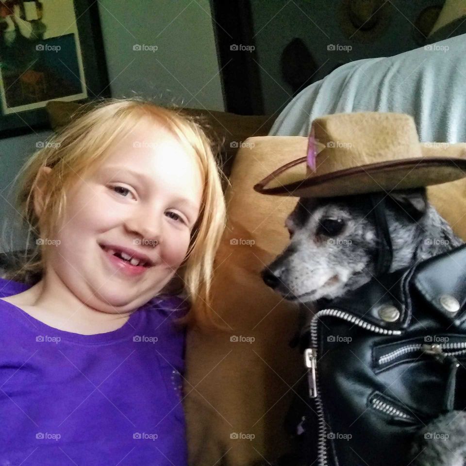 Girl admiring her pet dog with a leather jacket and a cowboy hat on