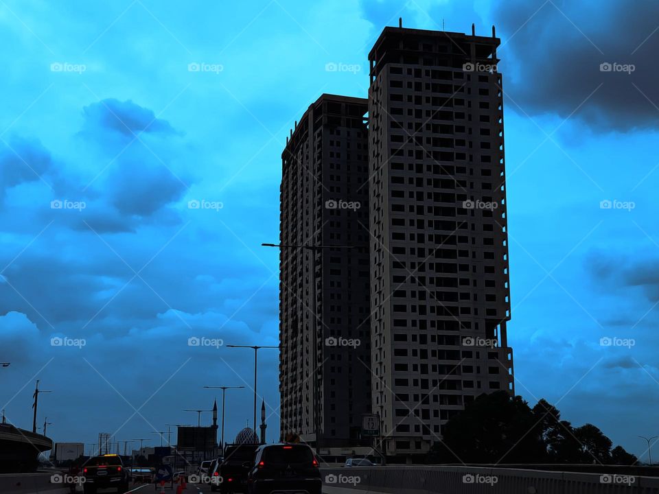 Two tall buildings, opposite the flyover, night view of flyover, cloud sky, overcast sky, city view, night city view, evehivle on the flyover are not stuck, flyover situation, only a few vwhicle passing,