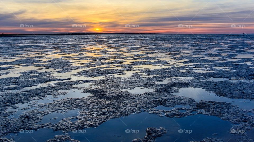 Sun rising over low tide mud flats of bay