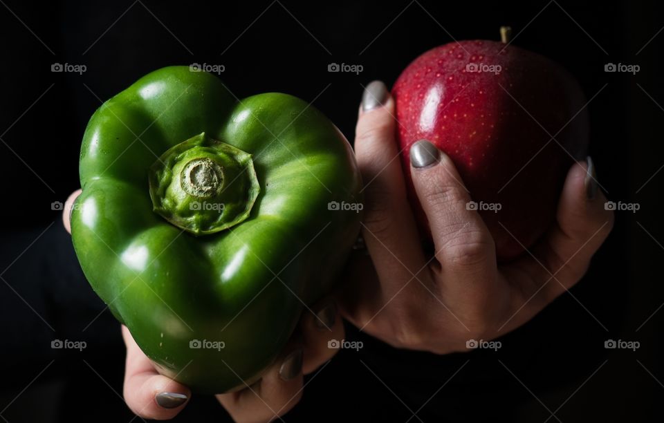 Hands holding a green pepper and red apple with a black background