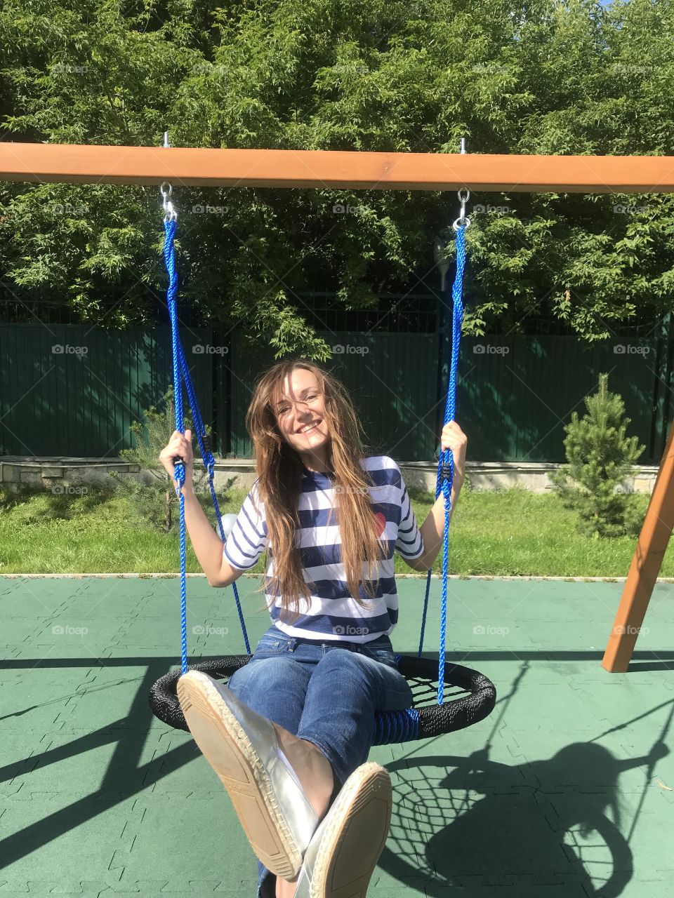 Laughing girl swinging on a swing. Long haired girl laughs. Girl in a striped T-shirt and jeans.