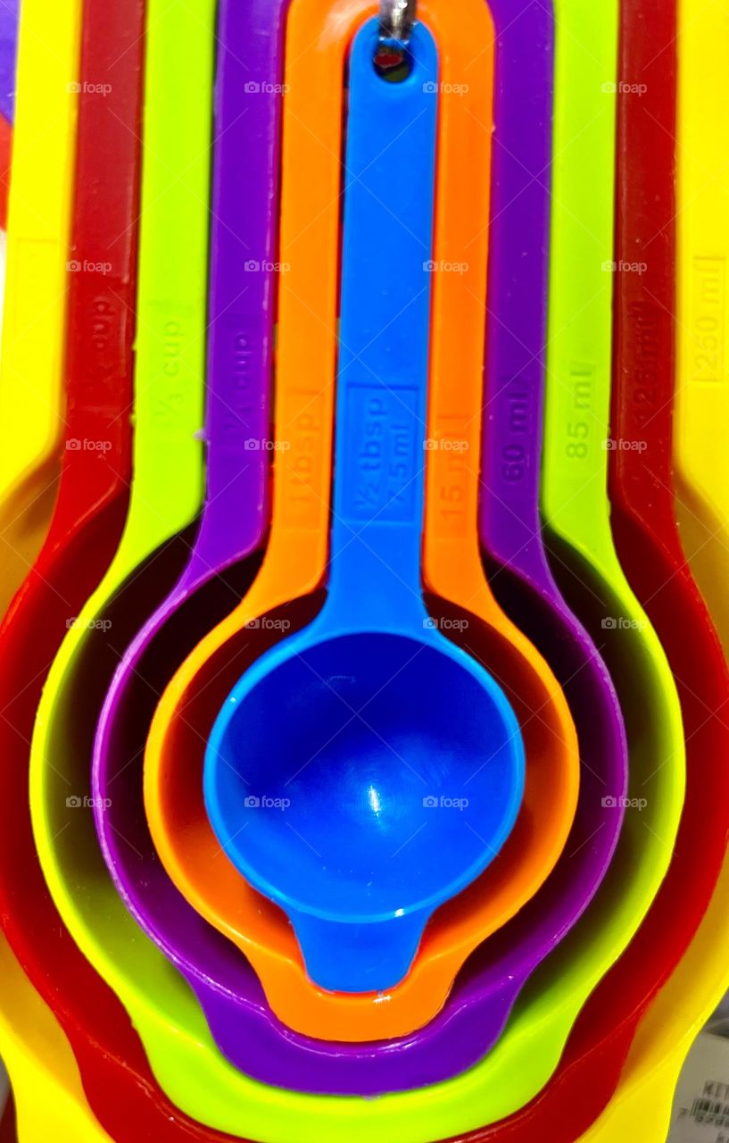 A vibrant set of measuring spoons in various colors, including blue, purple, orange, green and red, hanging in an organized way.