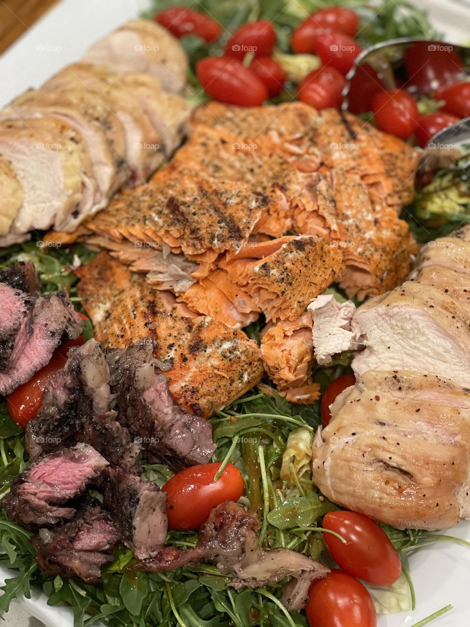 Freshly cooked salmon, steak, & chicken on a bed of colorful spring salad