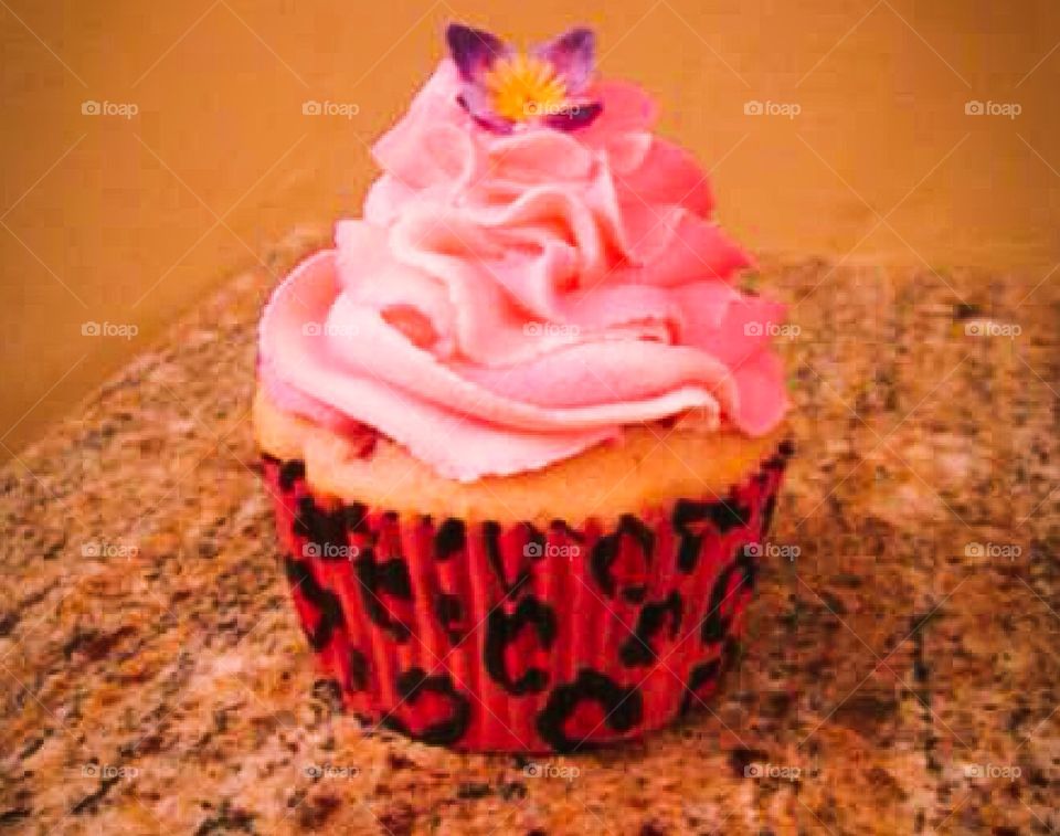 Beautiful pink icing swirled cupcake with a flower on top.