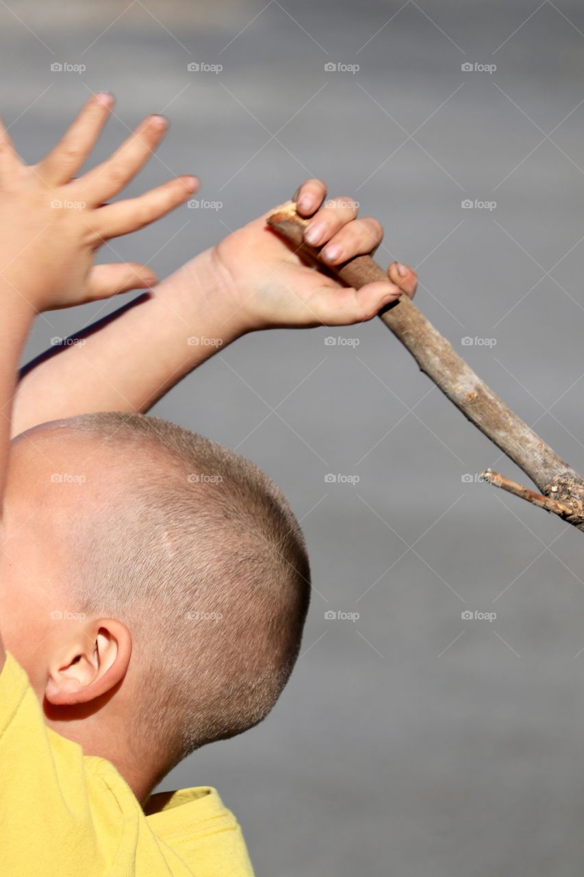 Four year old boy with stick in hand and raised over his head 