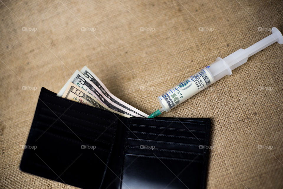 Syringe with one hunded dollar note inside injecting money in black wallet with some money