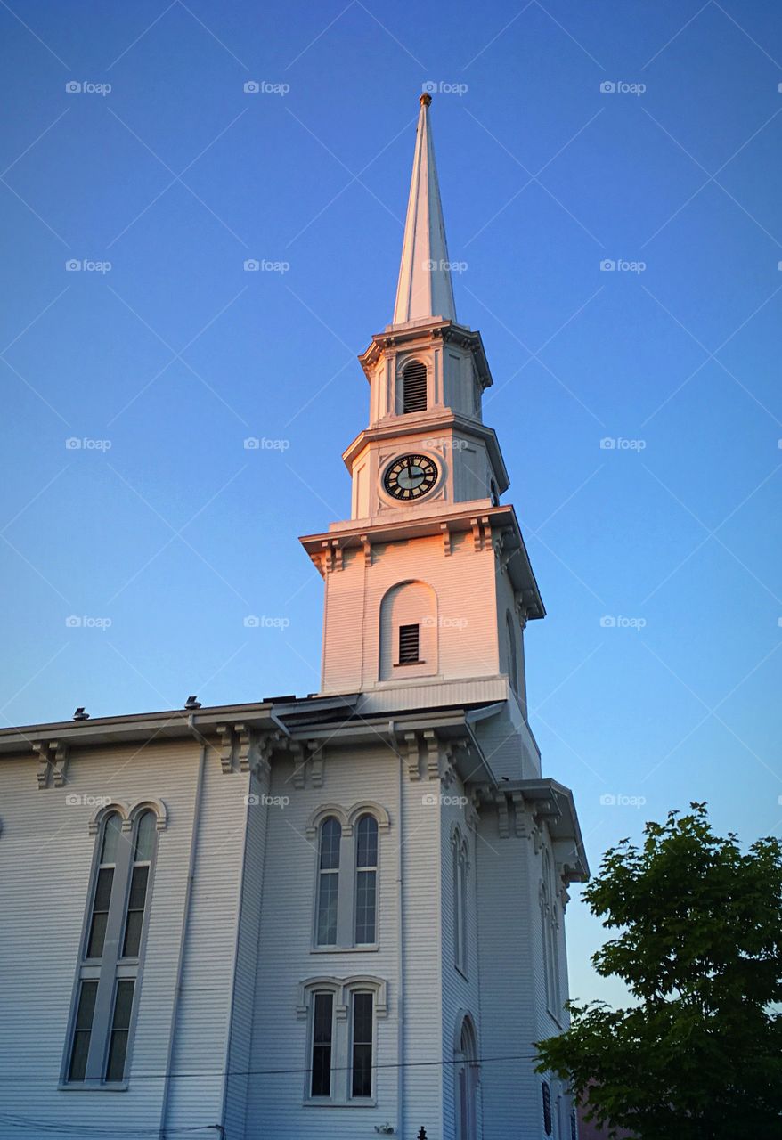 Looking up at the church steeple which looks beautiful against a clear blue sky and with the pink light of sunset. 