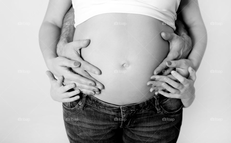Family of four, hands of mother, father and baby at tummy 