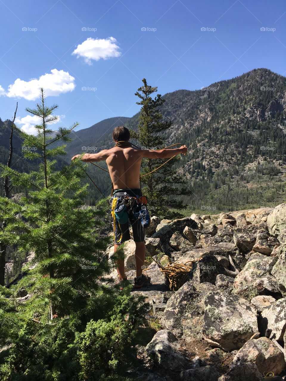 Shirtless rock climber sorting rope on a mountain 