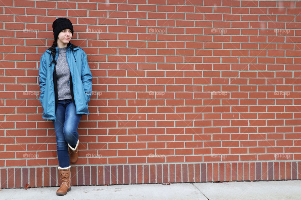 Young woman leaning against a brick wall