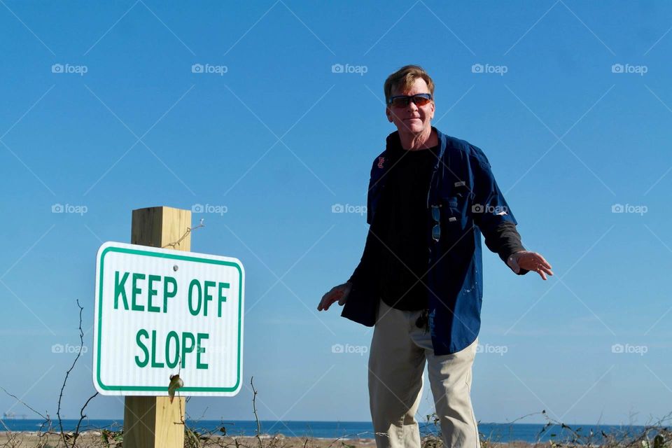 Man standing on a slope, next to a keep off slope sign