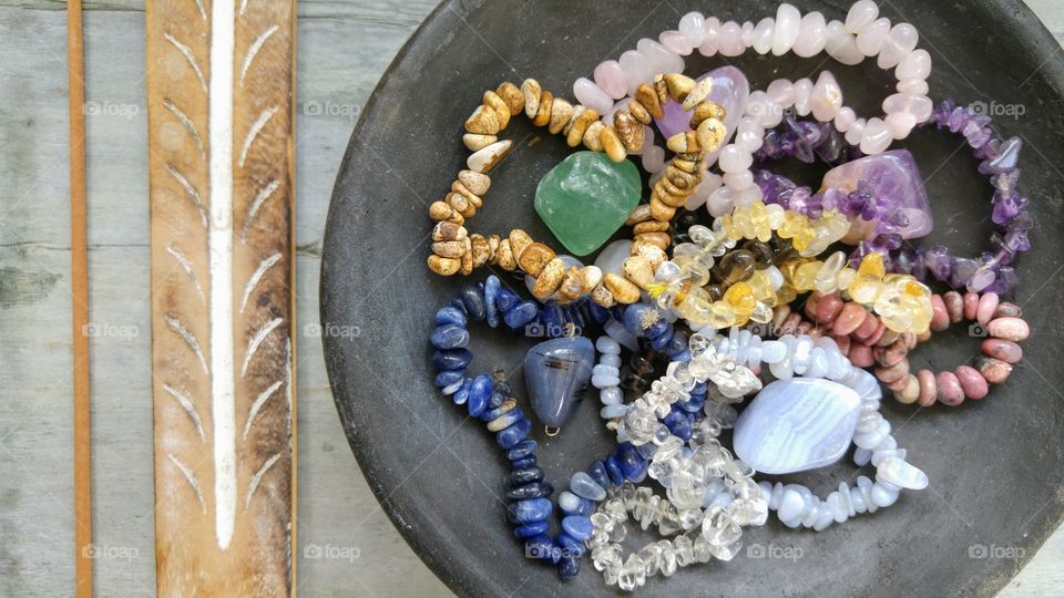 gem stones beads in a black bowl on a wooden background with incense