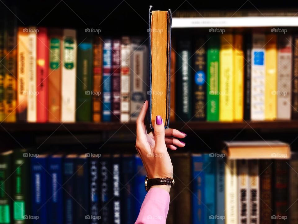 Female hand taking a book from the bookshelf 