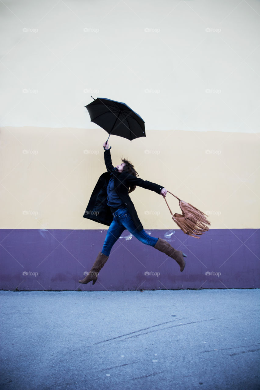 Woman with umbrella jumping against the colorful wall