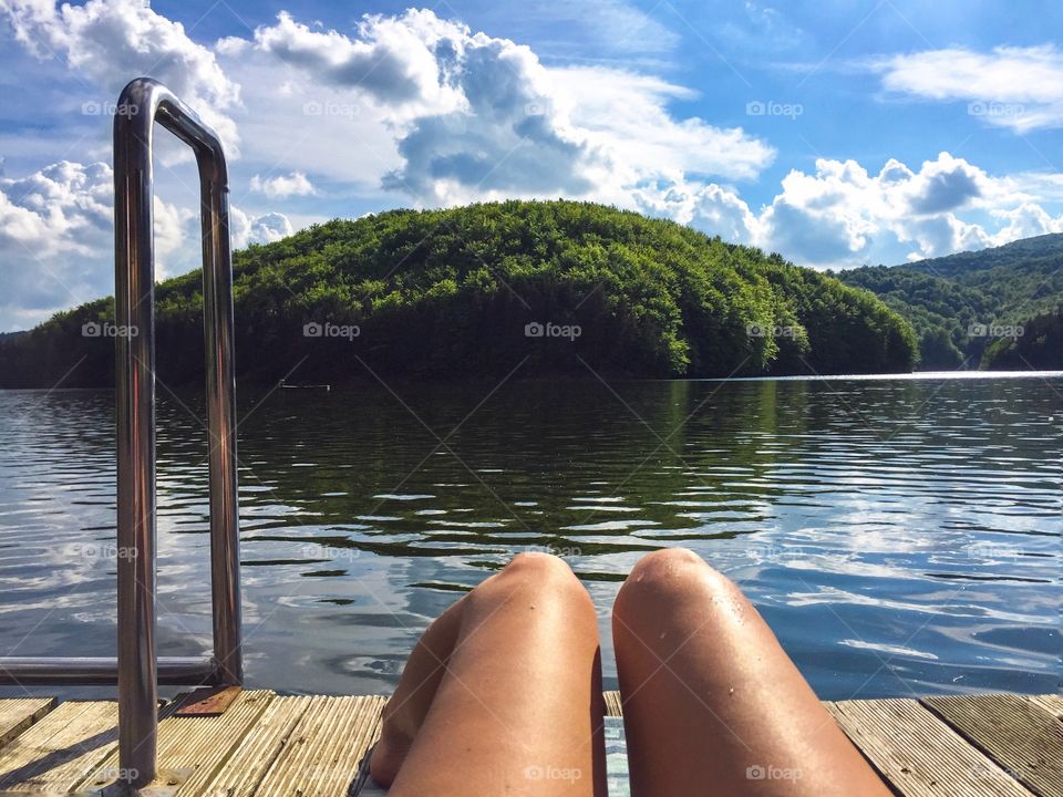 Let's get tanned - woman's legs and lake surrounded by forest 